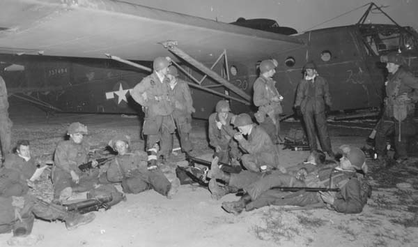 Francja, 24 marca 1945 roku – żołnierze piechoty szybowcowej amerykańskiej 17. DPD przed wejściem na pokłady szybowców. W tle szybowiec CG-4A-WO o wojskowym numerze seryjnym 43-37494. Szybowiec na podwoziu kołowym nie dopuszczonym do lądowań w terenie przygodnym. Kąt przodowania tego typu podwozia, krotki nos szybowca bliski środka ciężkości, nagminne i bezprawne zmuszanie dowódców szybowców USAAF do przewozu ładunków daleko przekraczających maksymalną dopuszczalną masę startową, a w konsekwencji złe wyważenie całej konstrukcji powodowały to, że ten typ podwozia stanowił idealną oś obrotu CG-4A do kapotażu – rzecz nieznana w wojskowym szybownictwie brytyjskim. Sekcja ogonowa tego konkretnego egzemplarza szybowca 43-37494 jest przystosowana do zainstalowania spadochronu hamującego, który mógłby zadziałać także jako element przeciwkapotażowy, lecz szybowiec nie ma tego spadochronu, gdyż przez całą wojnę dostarczano ich za mało. W czasie wojny amerykański miesięcznik techniki lotniczej „Air Tech” dwukrotnie pisał, że CG-4A musi lądować w warunkach bojowych normalnie, czyli na płozach, jak nakazywały to także instrukcje wykonywania lotów tym typem szybowca, ale europejskie USAAF nie zamówiły tzw. podwozia taktycznego dla CG-4A i lądowały tymi szybowcami w warunkach bojowym na tzw. podwoziu szkolnym, które widać na fotografii. Liczbę ofiar kapotaży CG-4A – czyli ofiar nie bojowych, poniesionych wyłącznie z winy urzędników – zatuszowano i wszystkie one występują w którejś z siedmiu kategorii strat bojowych. Fot. US Army